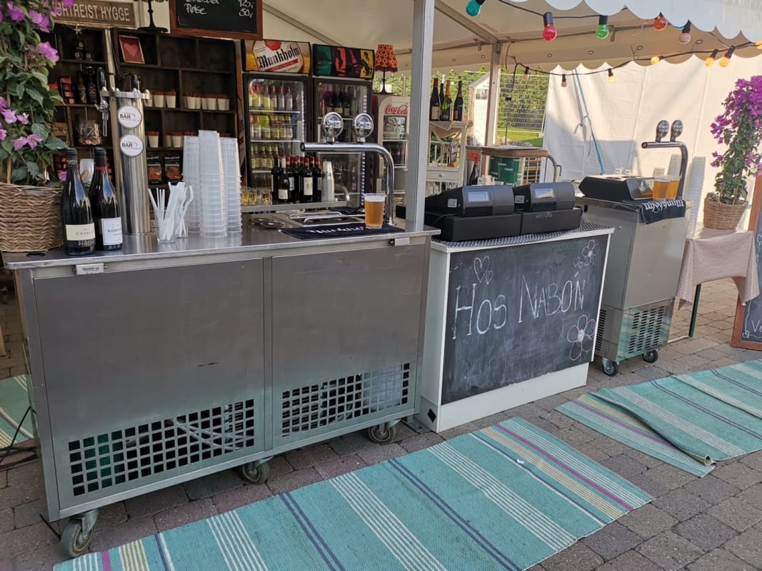 Servering fra tappetårn under festival, med gjester ved bardisken og ferdig tappet øl